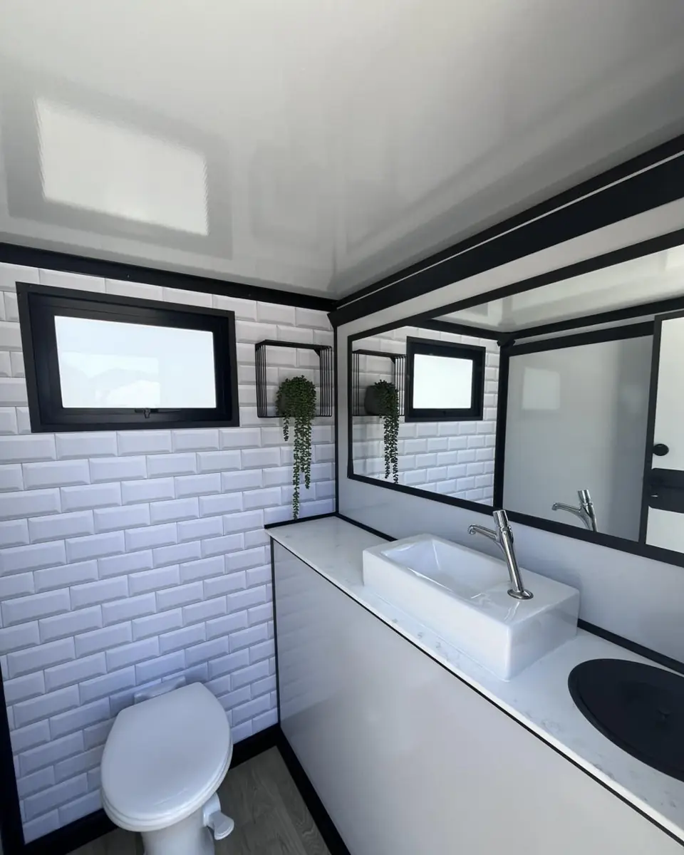Inside a restroom trailer with a white vanity sink, mirror, tiled wall and toilet