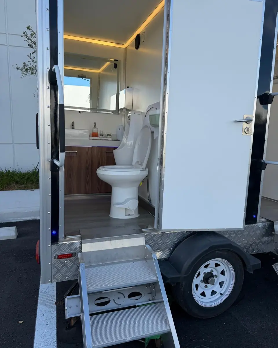 Restroom trailer stall door open showing the toilet and lit vanity