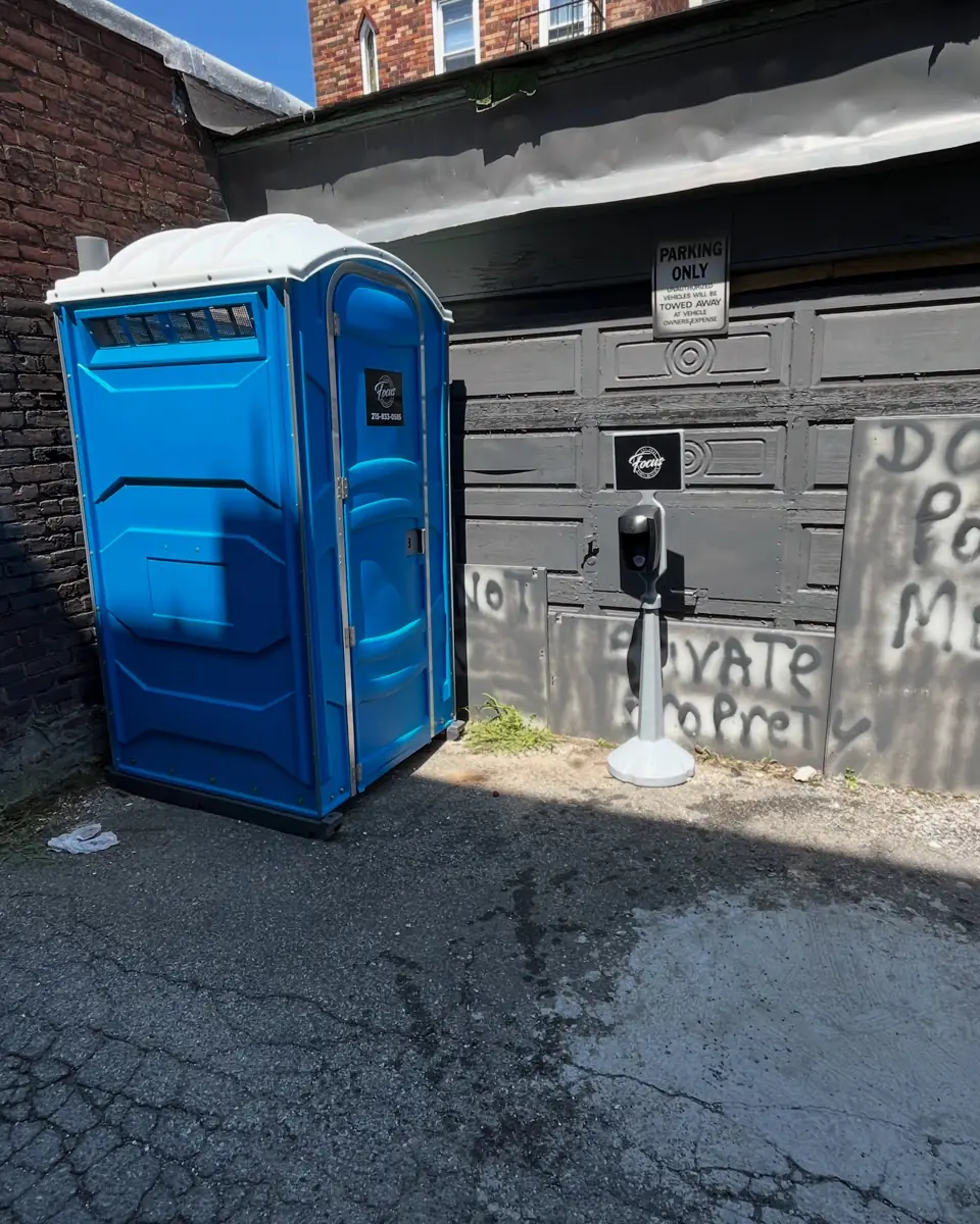 Blue portable toilet on a driveway next to a fence