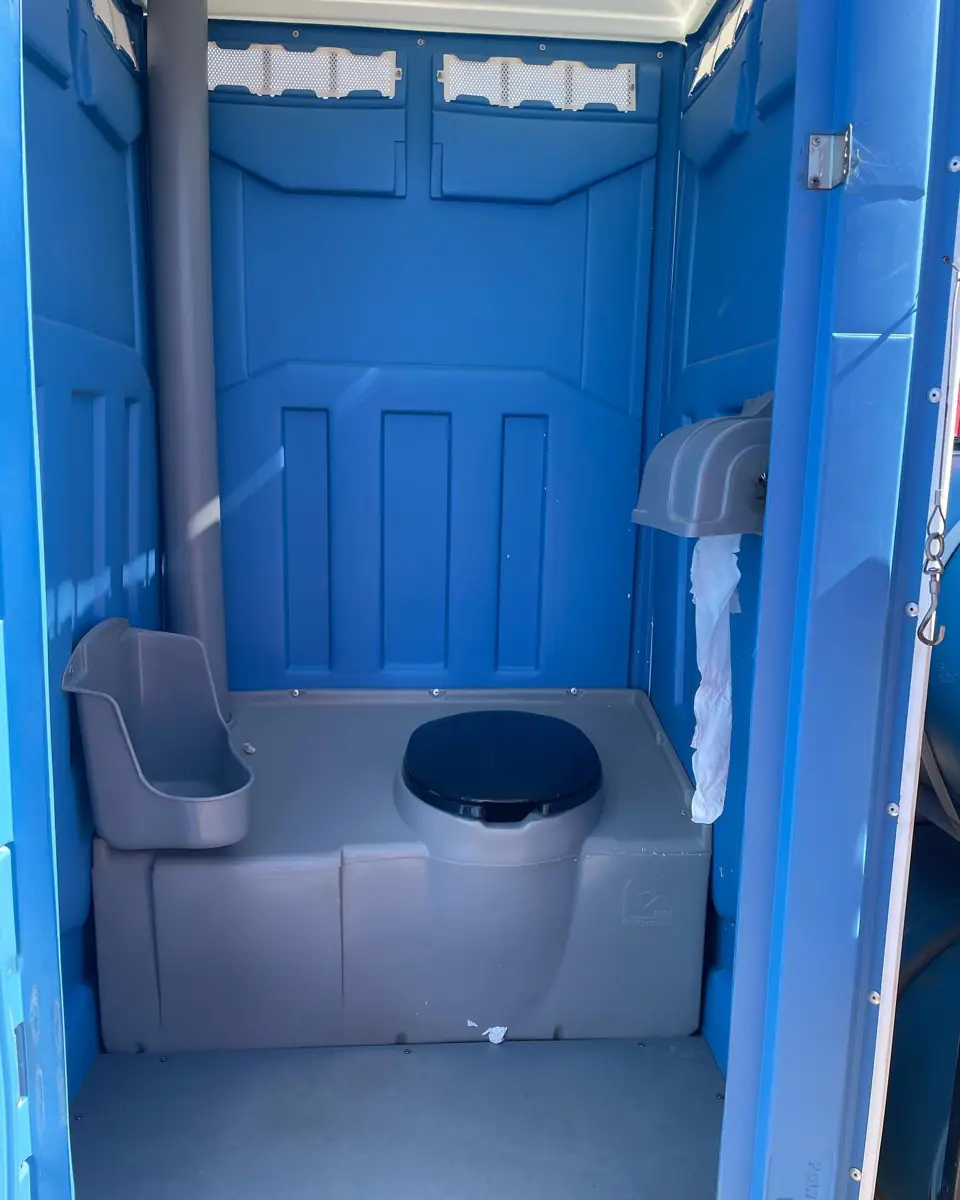 Inside a blue standard portable toilet showing the seat, urinal and vent pipe